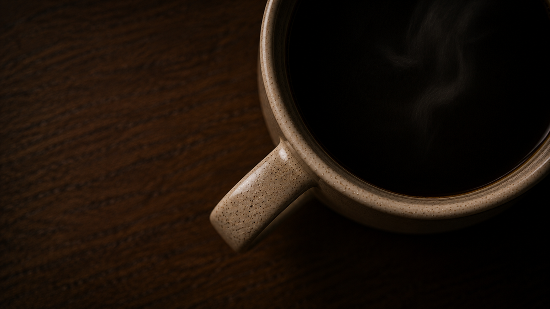 A top down view of a wooden desk with a cup of hot black coffee.