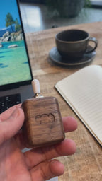 Focus Switch walnut desk fidget held in hand beside laptop, notepad and coffe, in a workspace cafe environment.
